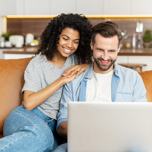 Happy couple lounging on couch surfing the web on their laptop.