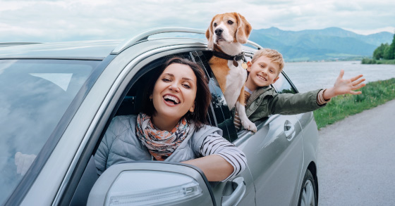 Woman and boy with a dog in a car by a lake, smiling.