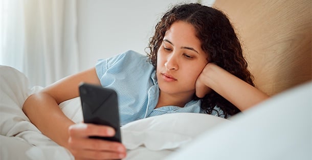 A woman lays in bed looking at her smartphone.